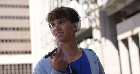 Young man talking into smartphone while wearing headphones on city street