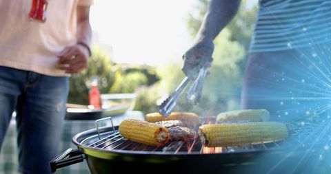 Grilling corn and burgers on kettle grill during backyard summer barbecue with friends