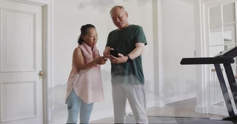 Mature couple sharing smartphone after home treadmill workout, promoting fitness together
