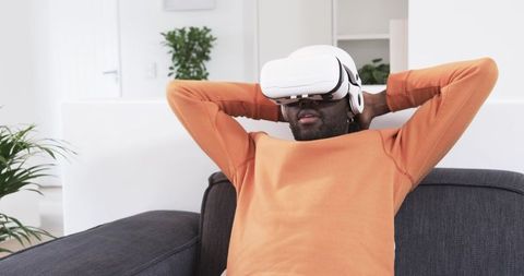 Relaxing African American man wearing VR headset on modern minimalist living room couch