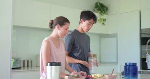 Couple preparing healthy fruit bowls on modern kitchen island