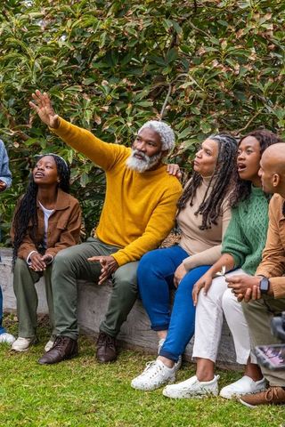 Multigenerational african american family pointing and watching phone in garden