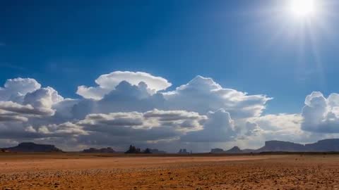 Sunlit storm clouds towering over arid desert plain with distant rock formations