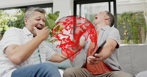 Mature men laughing on couch watching red globe graphic on tablet, casual home friendship