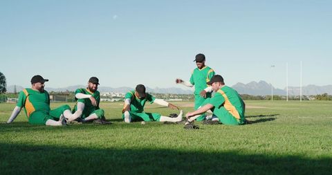 Teammates Stretching and Talking on Grass Field Wearing Green Uniforms and Black Caps