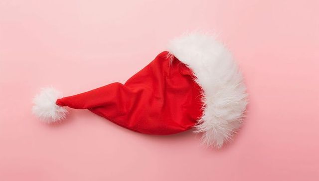 Red Santa Hat with Fluffy Faux-Fur Brim on Pastel Pink Background, Festive Holiday Prop