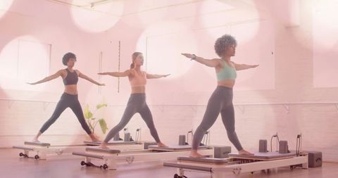 Women performing pilates reformer balance exercise in bright studio for core strength