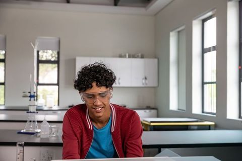 Teen male student working on laptop in school science lab wearing safety goggles