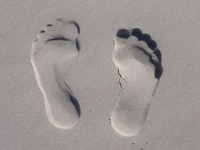 Footprints are engraved in soft white sand, highlighting the indentations and shadows created by bright sunlight. This captivating image can be used in travel promotions, vacation advertisements, and relaxation themes. Ideal for backgrounds, blog headers about beach vacations, or conceptual themes emphasizing traces and journeys.