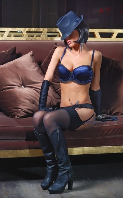 Seductive woman sits on sofa dressed in stylish lingerie, hat and high-heels, creating a confident and provocative ambiance. Ideal for fashion editorials, lifestyle blogs, adult content platforms, websites related to high-end lingerie brands, or promotional materials for nightlife events.
