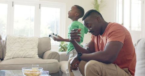 African American father and son playing video games on sofa at home laughing together