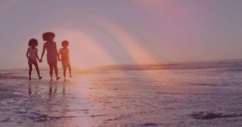 Mother walking with two children on wet sand at sunset casting reflections and lens flare