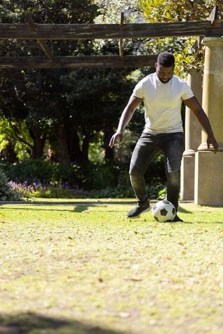 African man practicing soccer under pergola in sunlit park controlling ball on grass