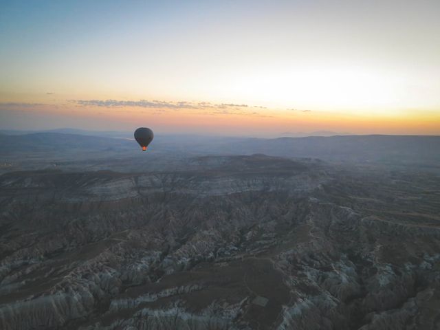 Hot air balloon floating over desert landscape at sunrise, capturing the peaceful beauty of the early morning. Ideal for travel advertisements, adventure blogs, serene landscape features, and promotional materials highlighting exploration and tranquility.