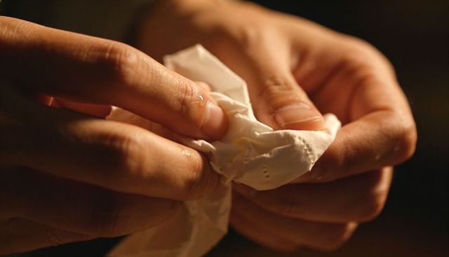 Crumpling tissue with moist fingertips closeup in warm amber light showing hand texture