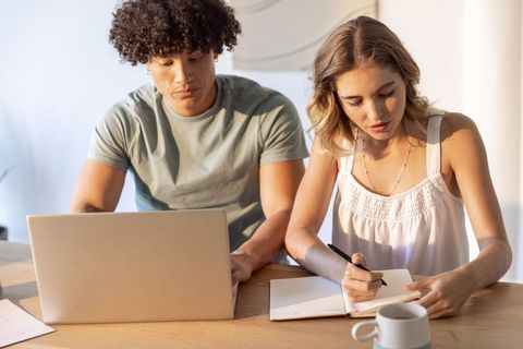Young couple studying and planning together, writing notes while using laptop on wooden desk