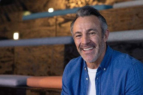 Middle-aged man smiling in cozy wood lounge wearing blue shirt, relaxed mature lifestyle