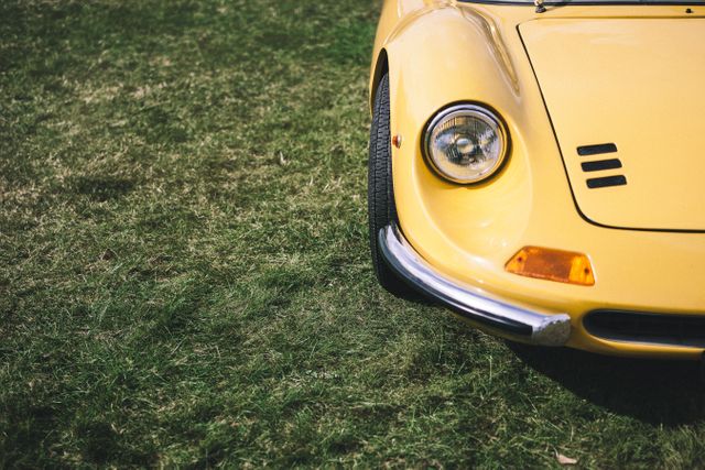 Image shows close-up of the front end of a yellow classic car parked on grass. Ideal for use in advertisements for vintage car events, automotive enthusiasts' blogs, car restoration promotional materials, and retro-themed marketing content.