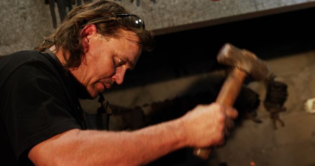 Picture featuring blacksmith hammering on metal. Great for use in content related to traditional crafts, metalworking techniques, artisan professions, vocational training, and labor-intensive occupations.