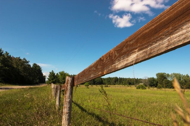 Rustic wooden fence standing along lush green meadow with clear blue sky in background. Ideal for themes related to countryside living, rural landscapes, nature, tranquility, farming, agricultural settings. Perfect for travel brochures, background images, environmental topics, and outdoor lifestyle content.
