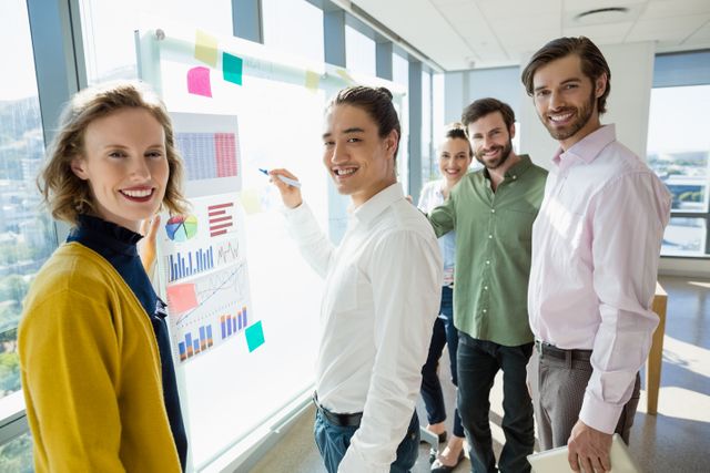 Group of business executives standing around a whiteboard with charts and graphs, smiling and collaborating. Ideal for depicting teamwork, corporate meetings, business strategy sessions, and professional environments. Perfect for use in business presentations, corporate websites, and marketing materials.