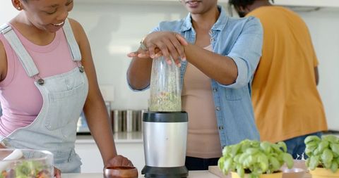 African american women blending green smoothie in modern sunlit kitchen with blender