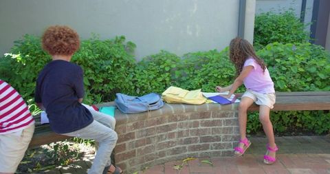 African American Children Studying Outdoors on Curved Brick Bench with Backpacks