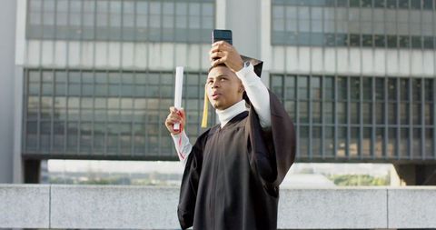 Urban graduate taking selfie on terrace holding diploma, celebrating graduation achievement