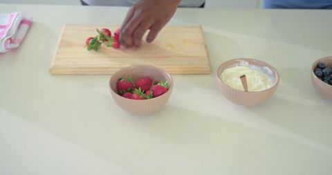 African american man arranging strawberries on wooden board with yogurt and blueberries