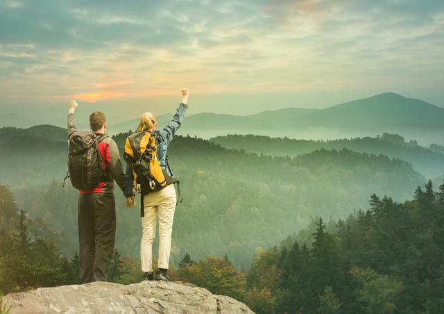 Two hikers celebrating on a mountain peak with arms raised in triumph at sunrise. Ideal for outdoor adventure, motivation, and tourism themes. Perfect for promotional materials, travel blogs, and inspirational presentations.