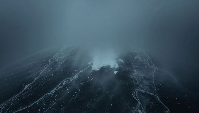 Drifting pale iceberg shedding fragments over foggy polar ocean with foam streaks