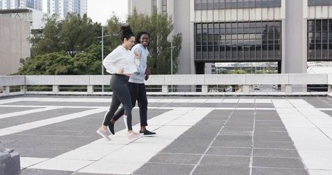 Jogging partners on urban rooftop terrace smiling and chatting while exercising