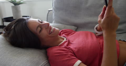 Smiling Woman Relaxing on Sofa Using Smartphone