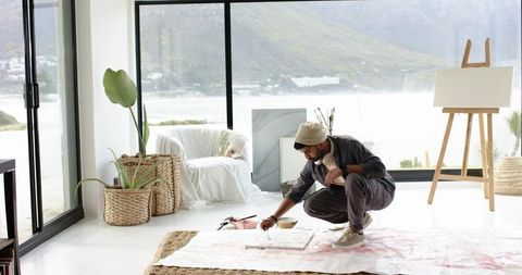 Indian artist painting on floor in sunlit minimalist waterfront studio with large windows