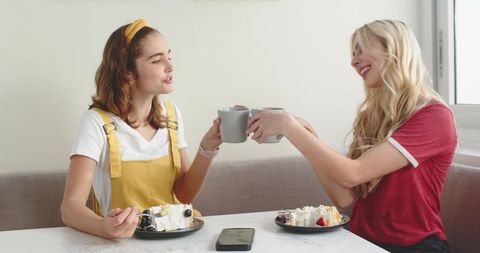 Friends toasting with coffee and cake in bright cozy dining nook, casual home moment