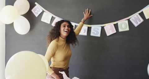 Smiling Woman Decorating Baby Shower Party with Balloons and Banner