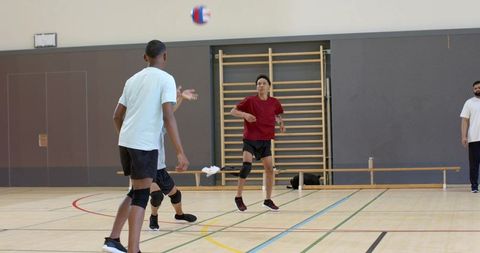 Teen male volleyball players passing ball in school gym practicing teamwork and agility