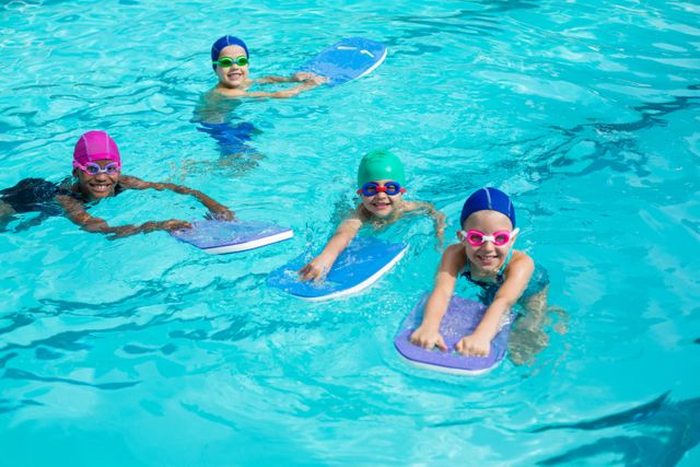 Children are enjoying their swimming lesson with kickboards in a pool. They are wearing colorful swim caps and goggles, indicating a fun and engaging learning environment. This image is perfect for promoting swimming lessons, summer camps, water safety programs, and children's sports activities.