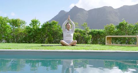 Asian Woman Meditating Outdoors by Pool with Mountains in Background
