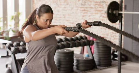 Asian woman performing battle rope workout in sunlit industrial gym for strength training