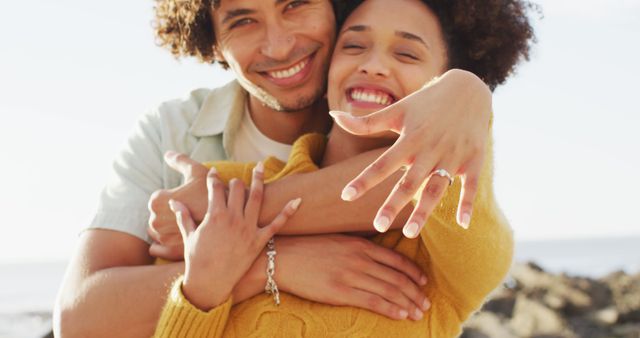 Portrait of african american couple smiling and showing their ring on the rocks near the sea. love and relationship concept