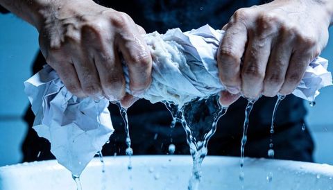 Adult hands wringing water-soaked cloth over basin dripping water squeezing tension