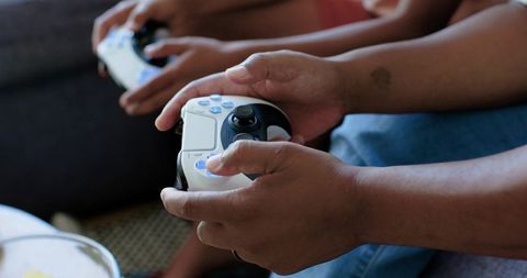 African american father and son playing video games, gripping white wireless controllers, close-up h