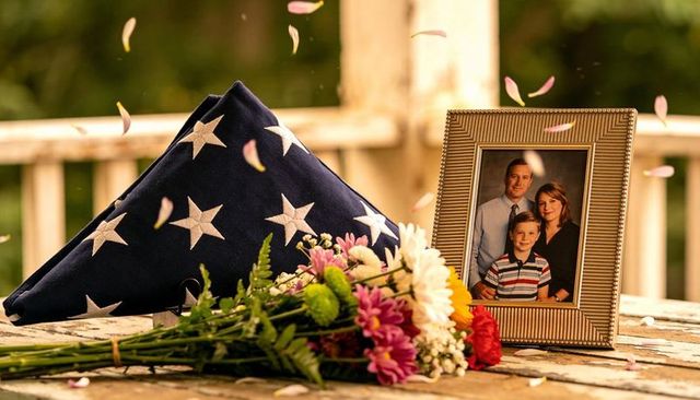 Folded american flag resting beside framed family portrait and bouquet on rustic porch