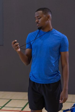 African american athlete standing on gym court holding stopwatch on lanyard in blue tee