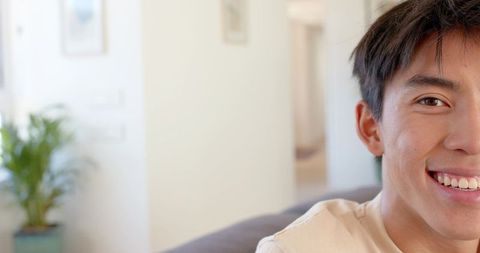 Smiling young asian man on gray sofa in bright living room with warm natural light
