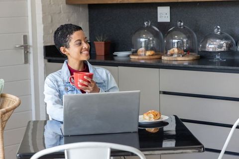 African american woman enjoying coffee while working remotely at modern kitchen table
