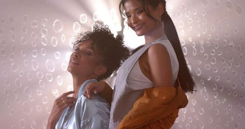 Diverse female duo posing in satin bomber and mustard jacket with warm lens flare