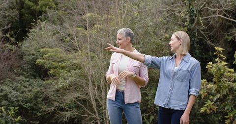 Two women standing in park pointing left and smiling, casual denim shirts, outdoor lifestyle
