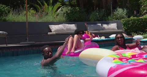 African american friends relaxing on colorful inflatable floats, lounging poolside outdoors